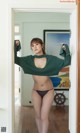 A woman in a green sweater and black bikini standing in a doorway.